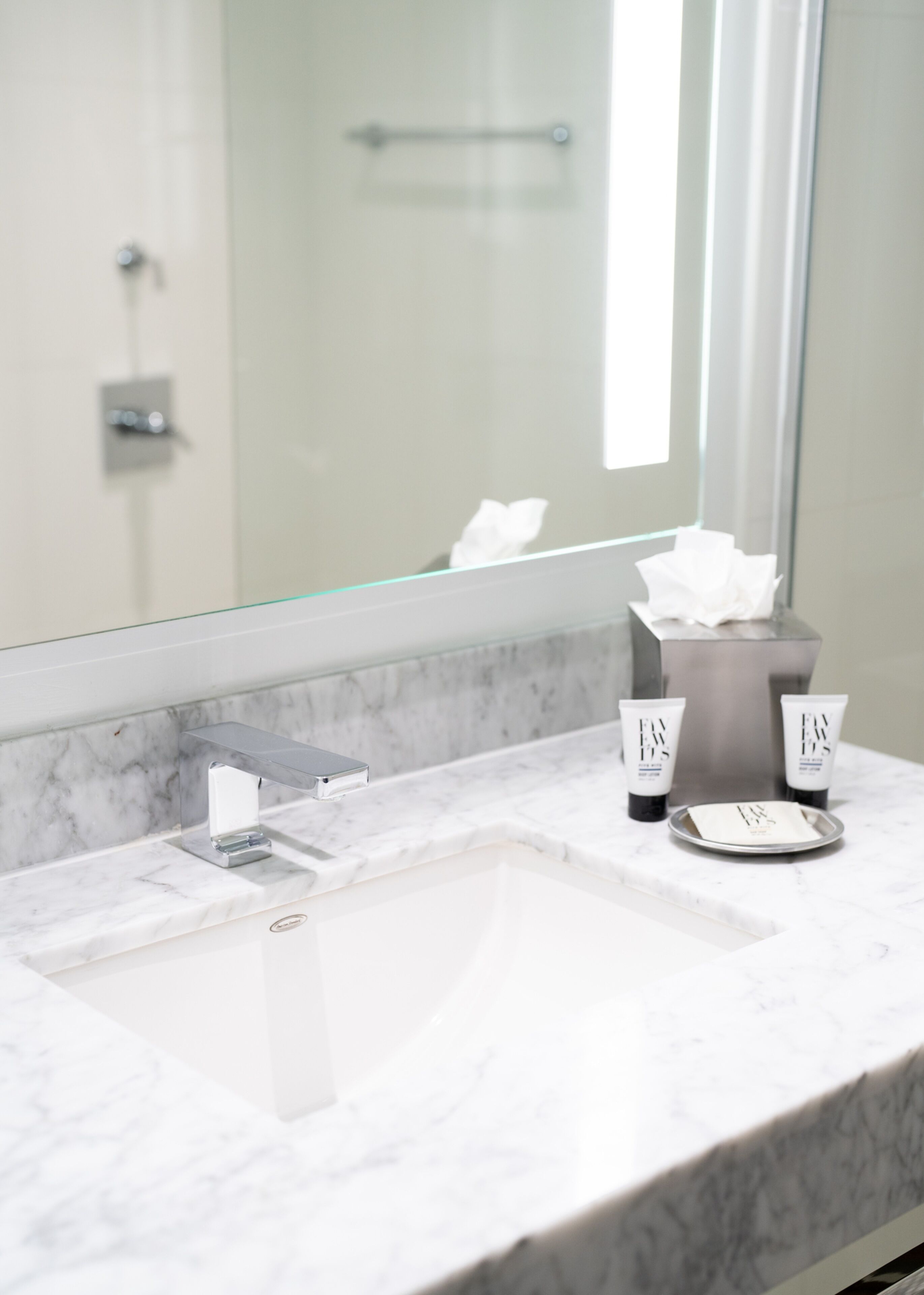 A bathroom with a marble sink, a mirror, and toiletries on the counter.