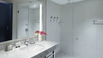 A modern bathroom with a marble sink, a large mirror, a glass shower enclosure, and a tiled floor.