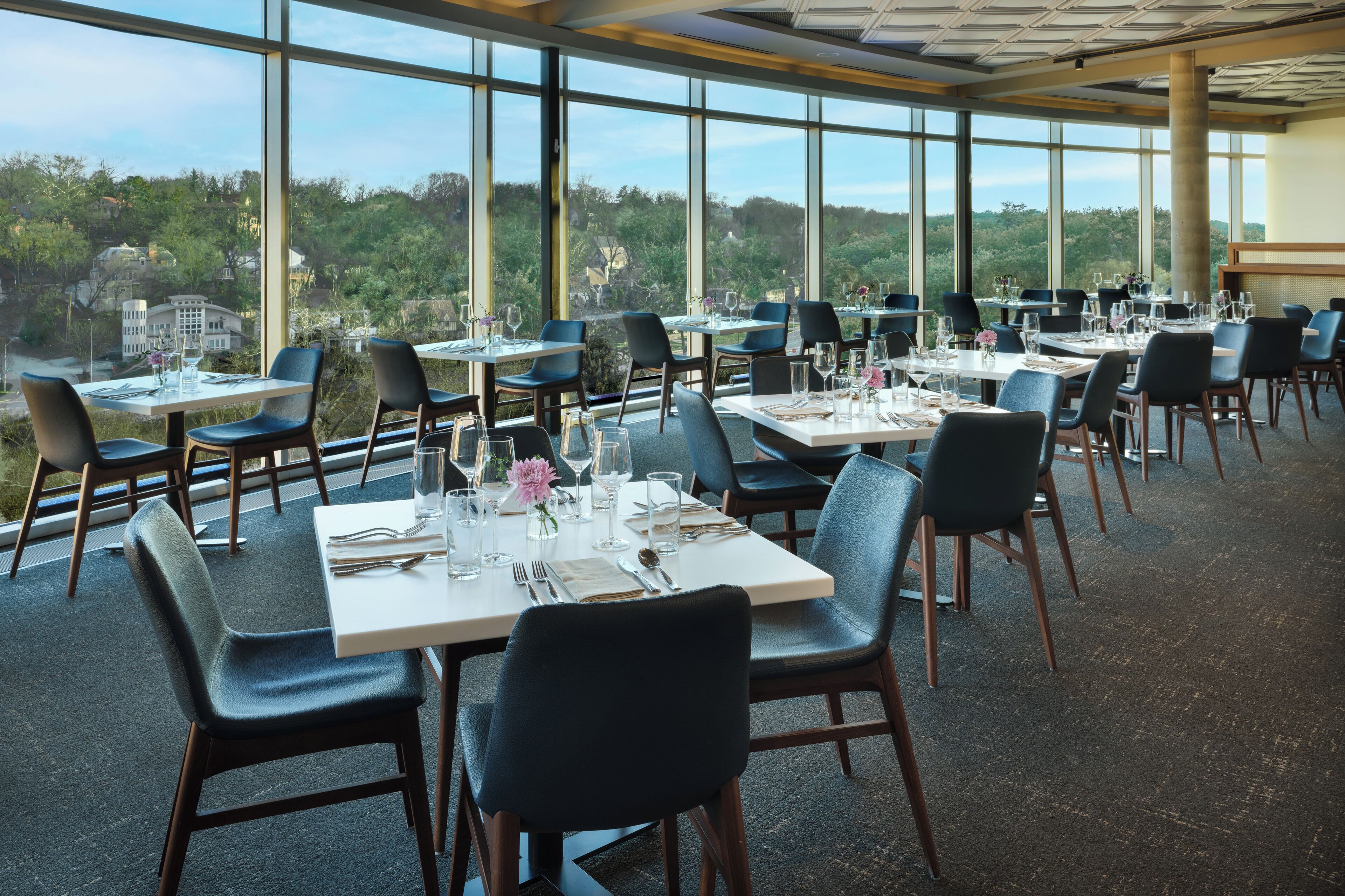 A restaurant with tables set for dining, large windows, and a view of the outdoors.