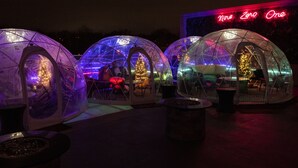 Transparent dome-shaped structures with seating inside, illuminated by colorful lights, and a neon sign in the background. - The Fontaine (Kansas City)