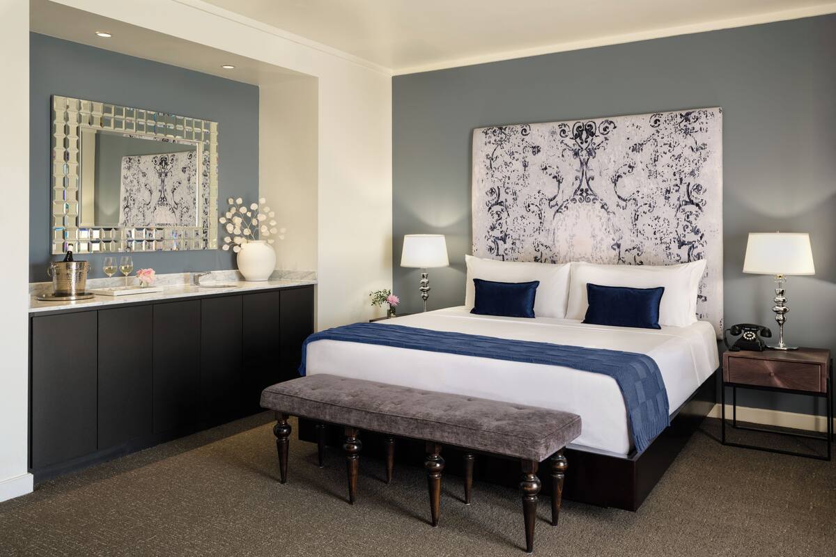 A bedroom with a large bed, bedside tables, a bench, a dresser, and a mirror.