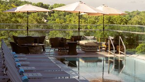 An outdoor pool area with lounge chairs, umbrellas, and a fire pit. - The Fontaine (Kansas City)