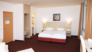 A hotel room with a double bed, two bedside tables, a desk, a chair, and a shower area.