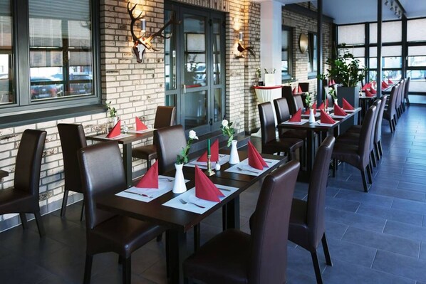 Un restaurante con paredes de ladrillo, sillas de cuero y mesas dispuestas con servilletas rojas y jarrones blancos.