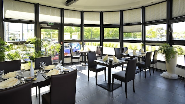 A restaurant with large windows, black chairs, and tables set for dining.