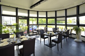 A restaurant with large windows, black chairs, and tables set for dining. - Hotel Quickborn (Quickborn)