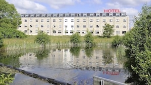 A hotel with a large building, a water body in front, and trees around.