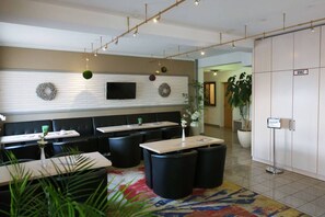 A modern hotel lobby with a seating area, a flat-screen TV mounted on a wall, and a reception desk. - Hotel Quickborn (Quickborn)