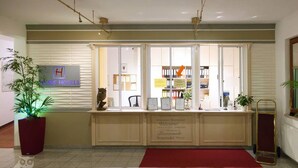 A reception desk with a sign for Hesse Hotels, a red carpet, and a potted plant.