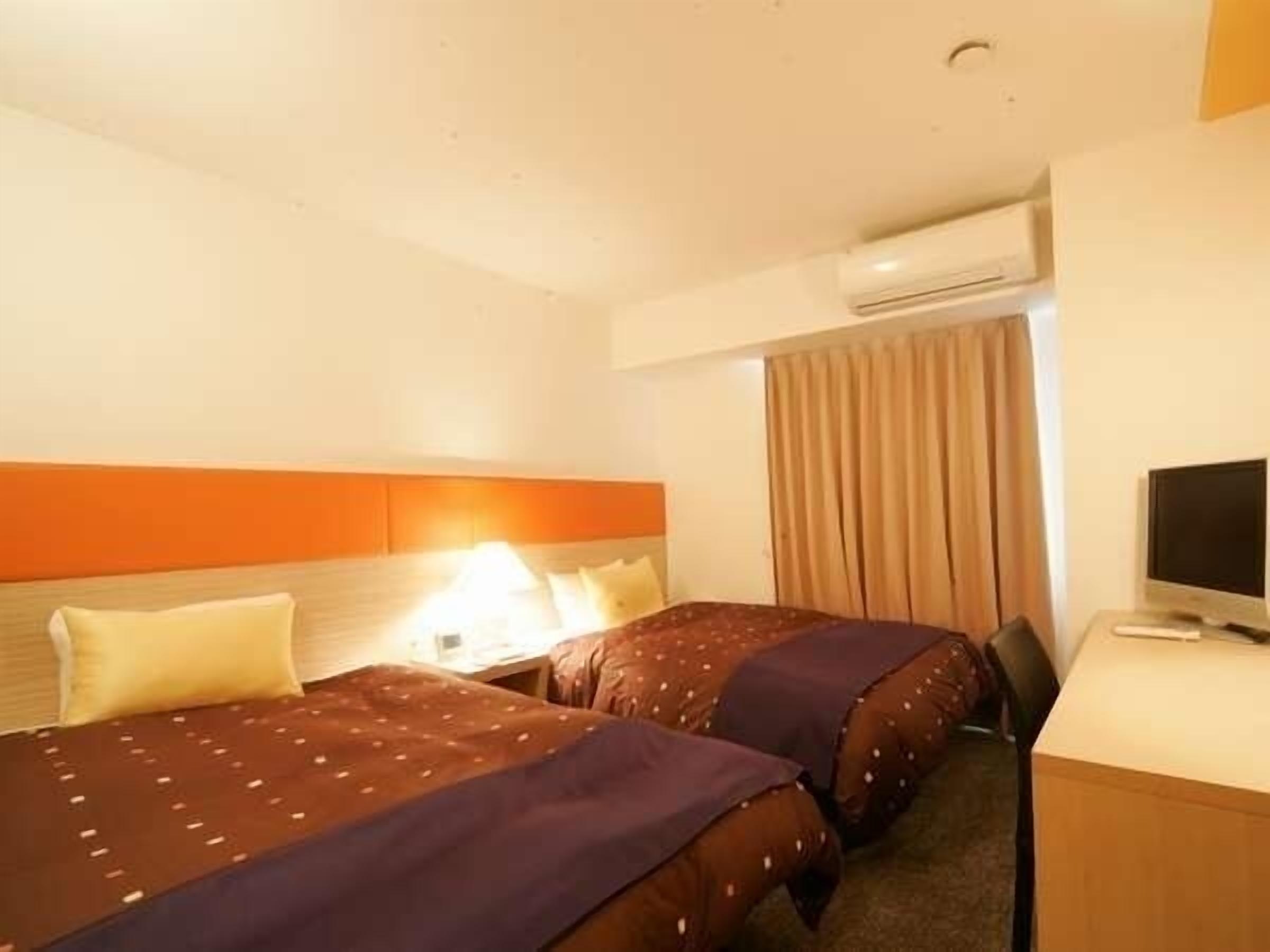A hotel room with two beds, a desk with a computer, and a TV.