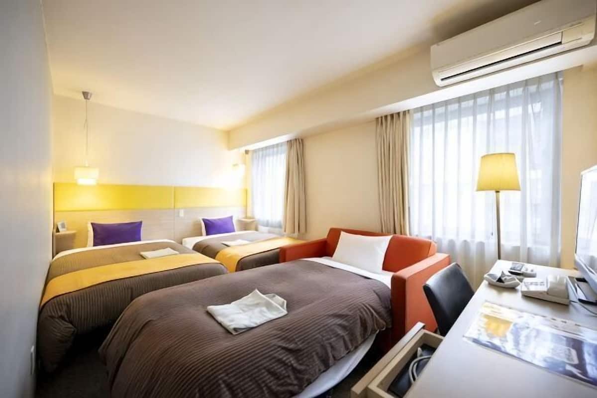 A hotel room with two beds, a desk, a chair, a lamp, and an air conditioning unit.