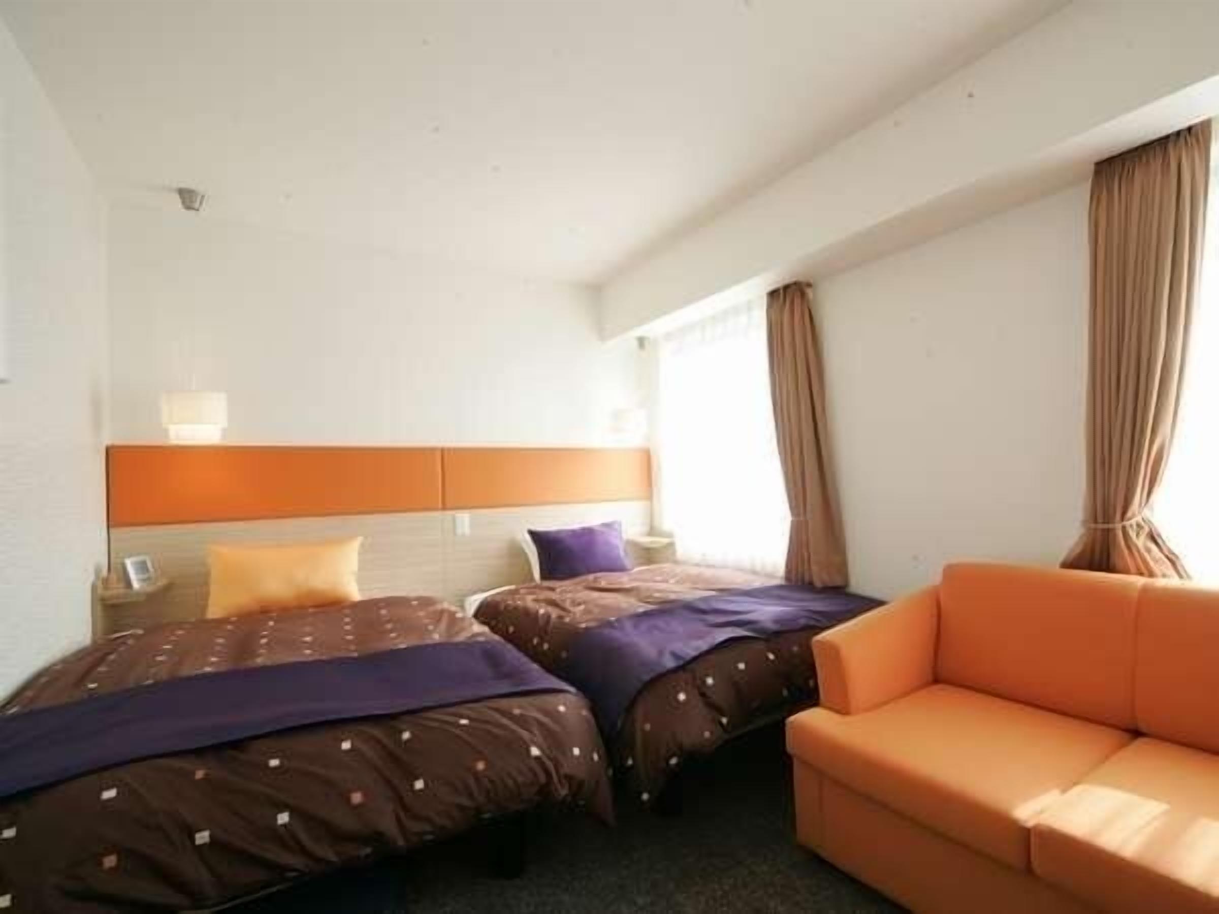 Una camera d'albergo con due letti, un divano e una finestra con tende.