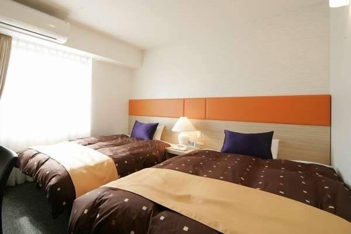 A hotel room with two beds, each with a headboard, a bedside table, and a lamp.