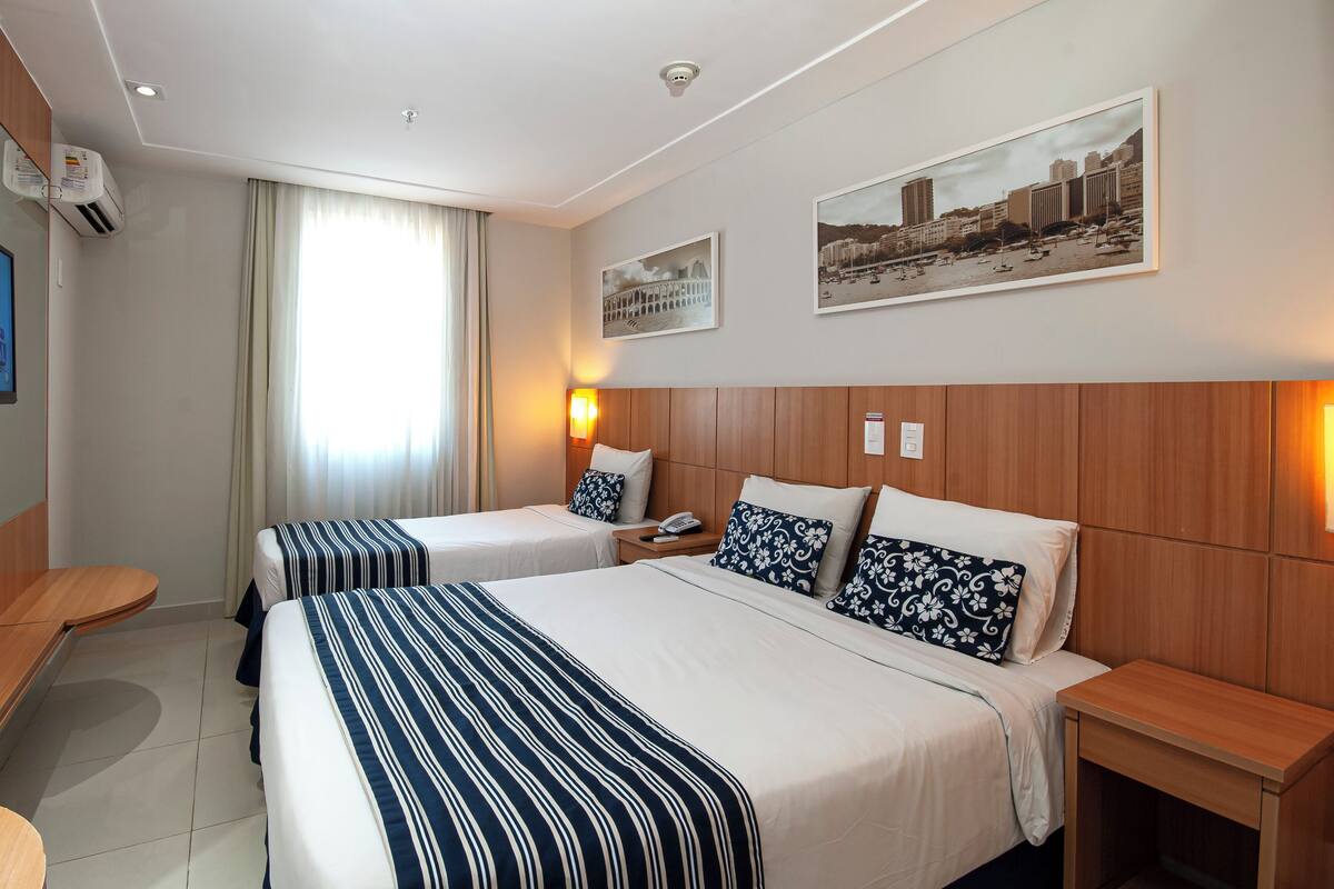 A hotel room with two beds, a TV, a painting, and a window with curtains.