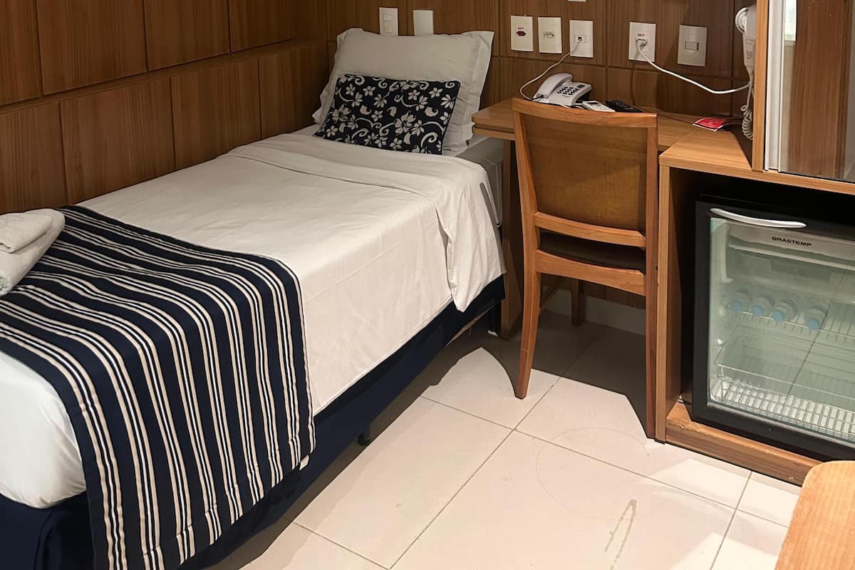 A hotel room with a bed, a desk with a telephone, an air conditioner, and a television.