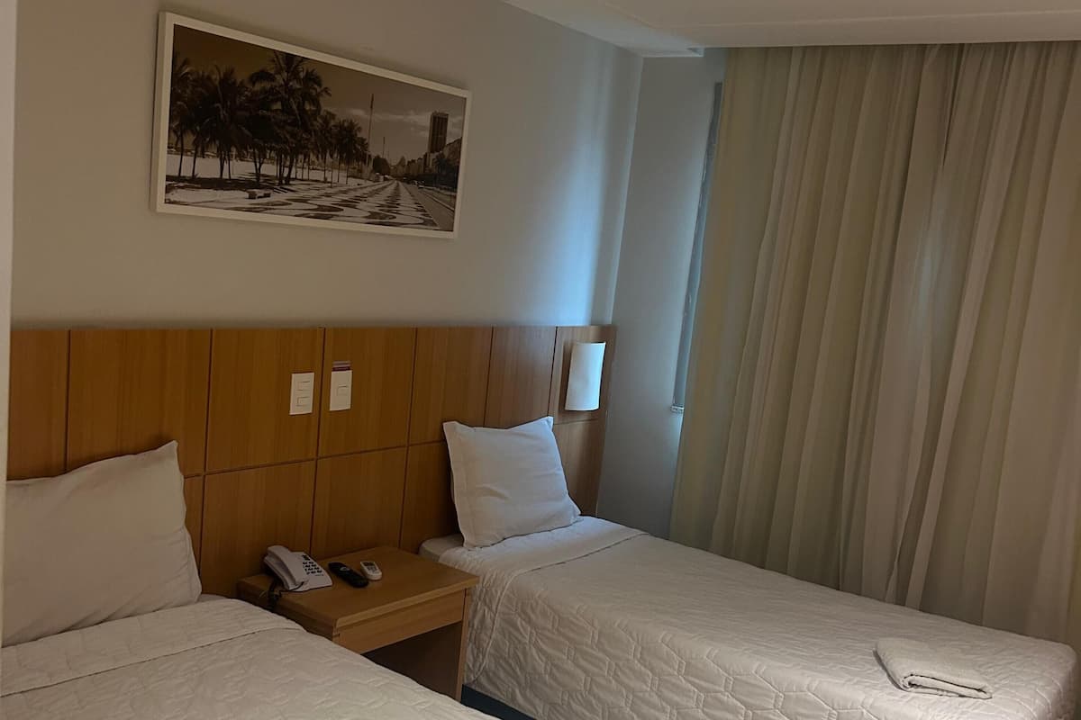A hotel room with two beds, a wooden headboard, a nightstand with a phone, and a painting on the wall.
