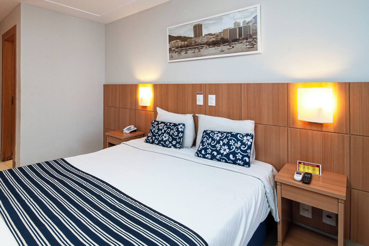 A hotel room with a large bed, two bedside tables, a nightstand with a phone, and a wall-mounted light.
