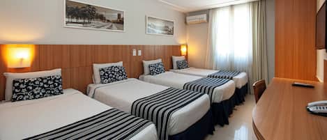 Habitación de hotel con cuatro camas, cabecera de madera, dos lámparas de pared, un televisor de pantalla plana y una mesa de comedor.