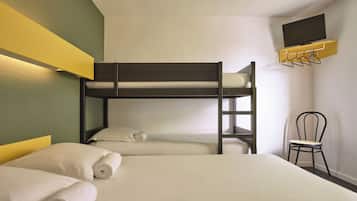 Quarto de hotel com cama beliche, uma cama de solteiro, uma cadeira, TV fixada numa estante e TV montada na parede.