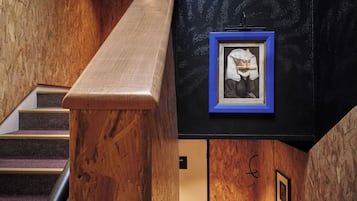 Una escalera de madera con una pared negra en la parte superior, que presenta un cuadro enmarcado y una pequeña señal.