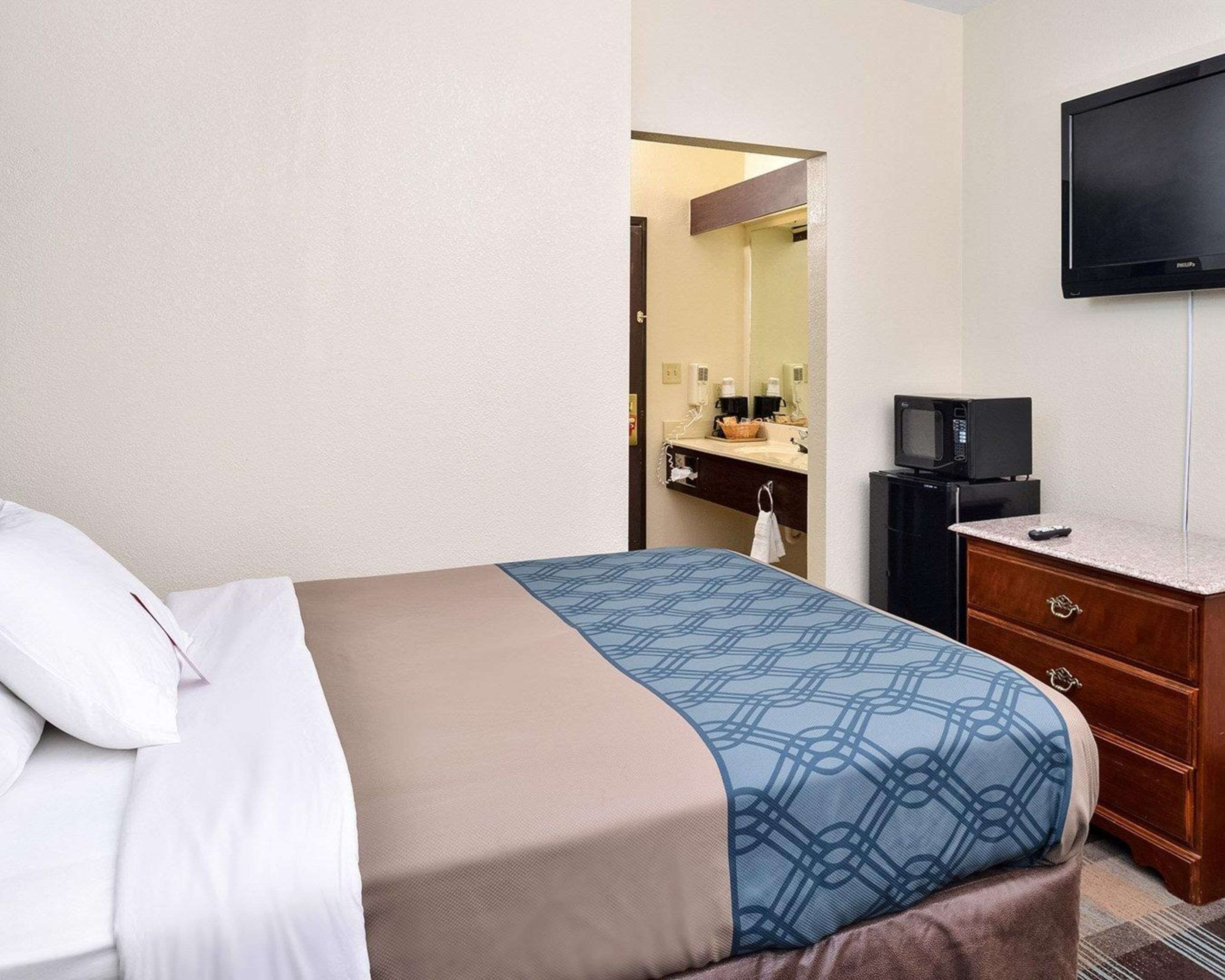 A hotel room with a bed, a dresser, a television, and a bathroom visible through an open door.