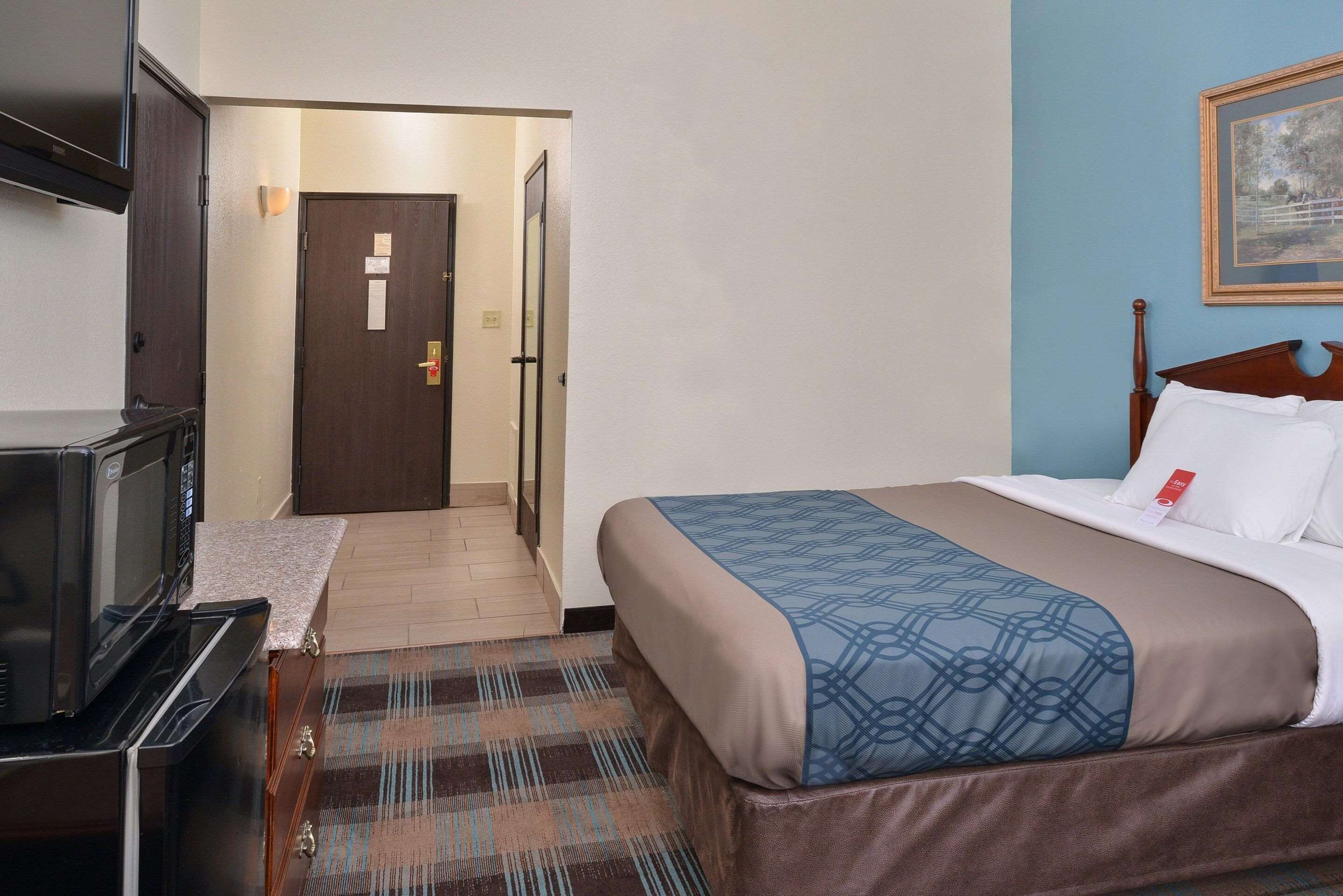 A hotel room with a bed, a television, a microwave, and a door leading to another room.