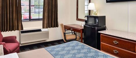 Quarto de hotel com uma cama, uma escrivaninha com computador, televisão e micro-ondas.