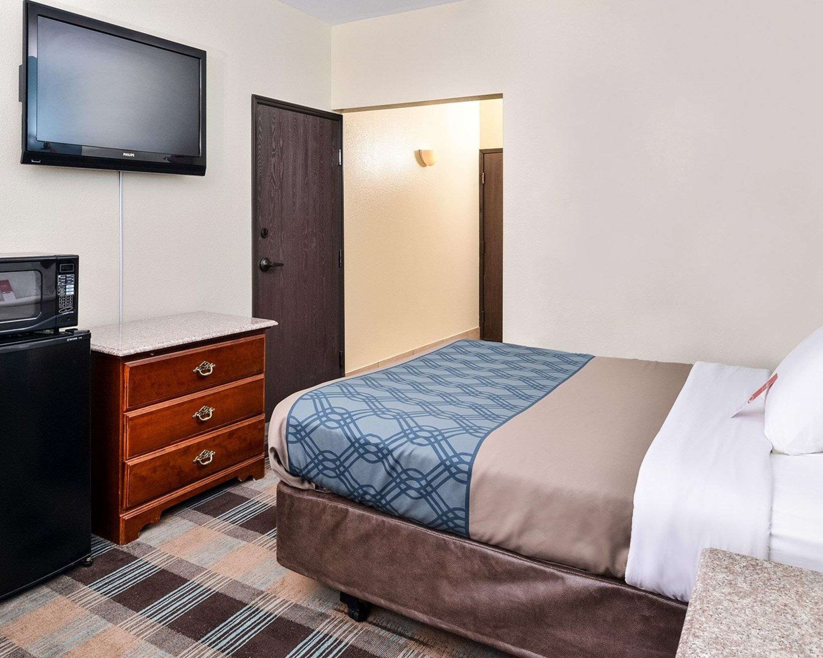 Una habitación de hotel con una cama, un aparador, un televisor montado en la pared y una puerta.