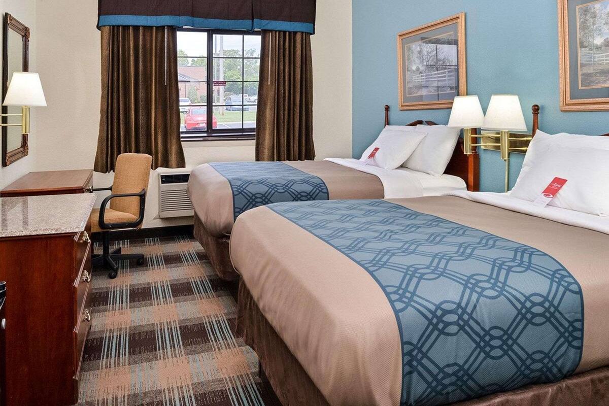 Une chambre d’hôtel avec deux lits, un bureau, une chaise et une fenêtre avec des rideaux.