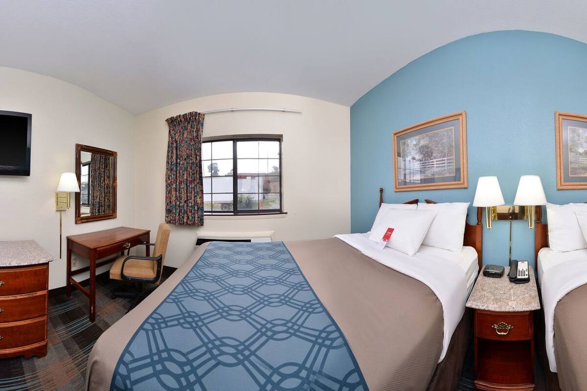 Une chambre d’hôtel avec deux lits, un bureau, une chaise, une télévision et un four à micro-ondes.