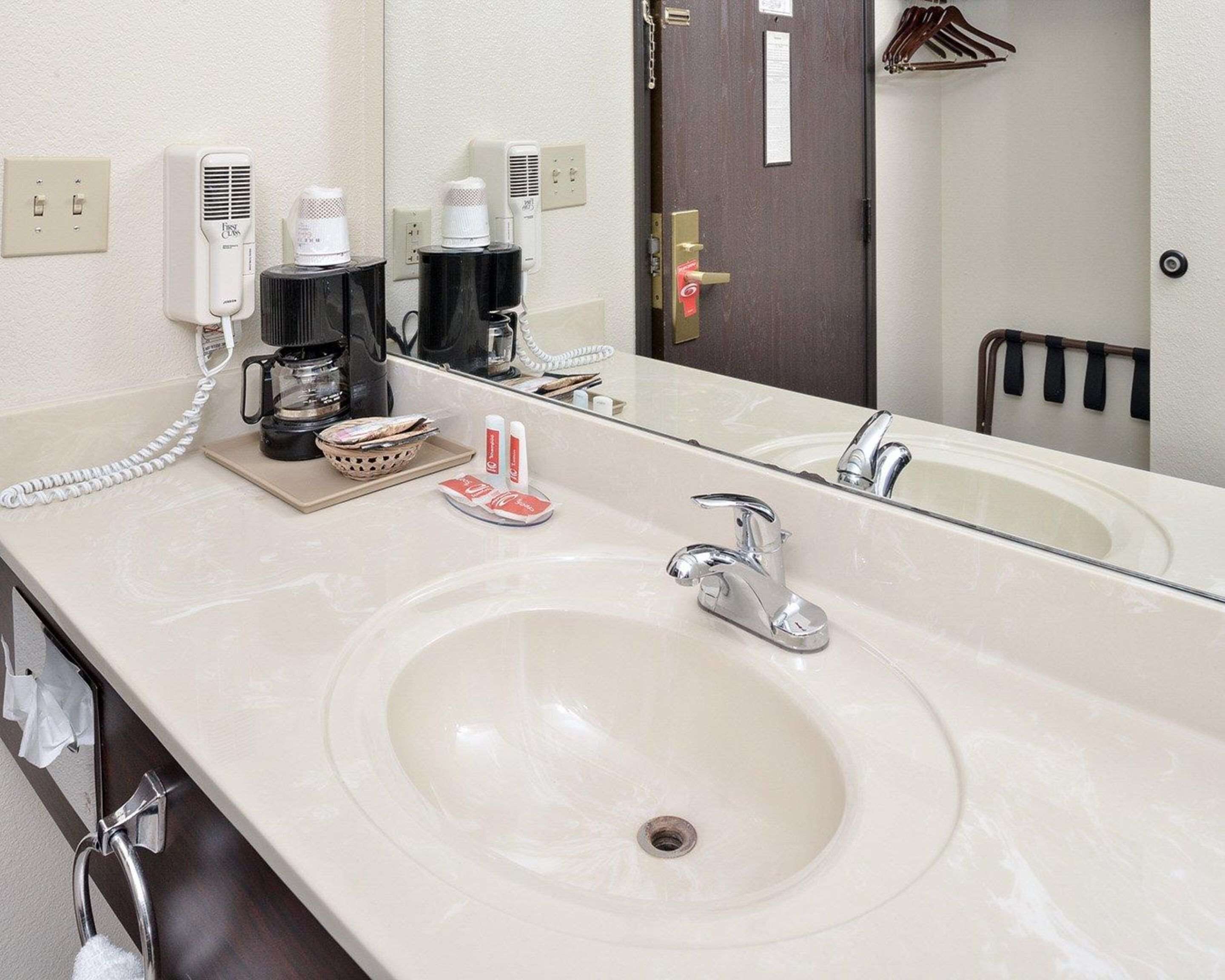 A hotel bathroom with a large sink, a mirror, a coffee maker, and a telephone.