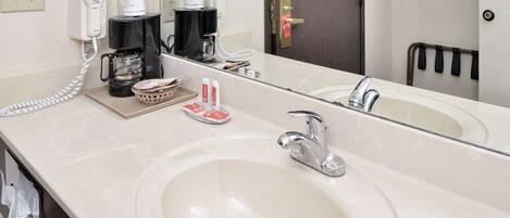 A hotel bathroom with a large sink, a mirror, a coffee maker, and a telephone.