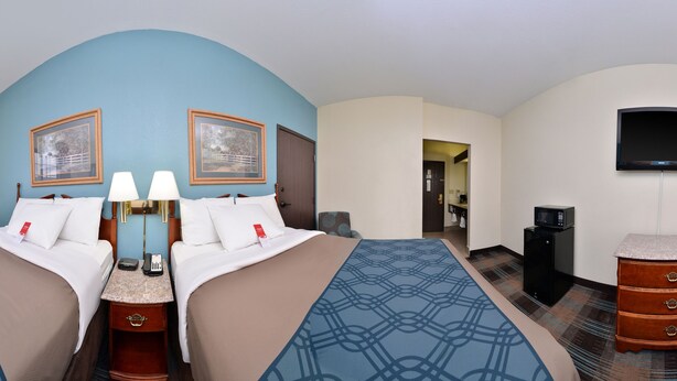 Quarto de hotel com duas camas, uma escrivaninha, uma cadeira, uma televisão e um micro-ondas.