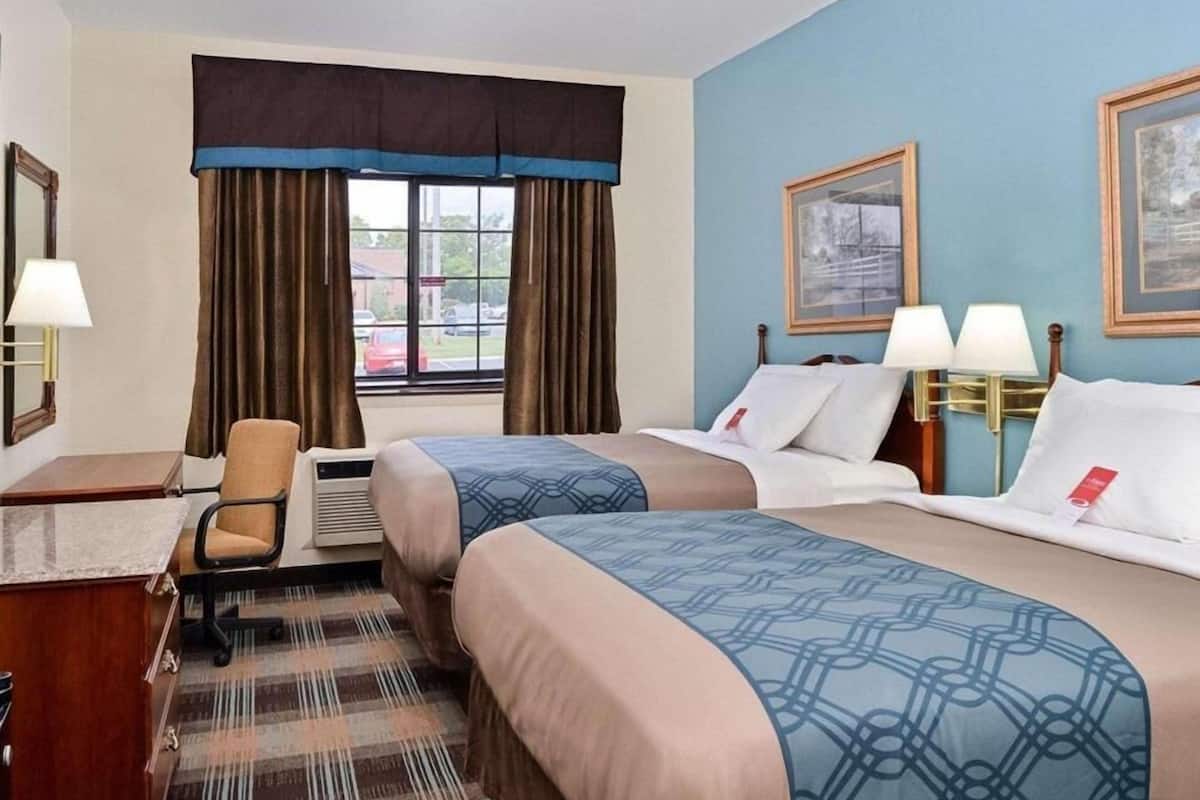 Une chambre d’hôtel avec deux lits, un bureau, une chaise, une fenêtre avec des rideaux et deux lampes fixées au mur.