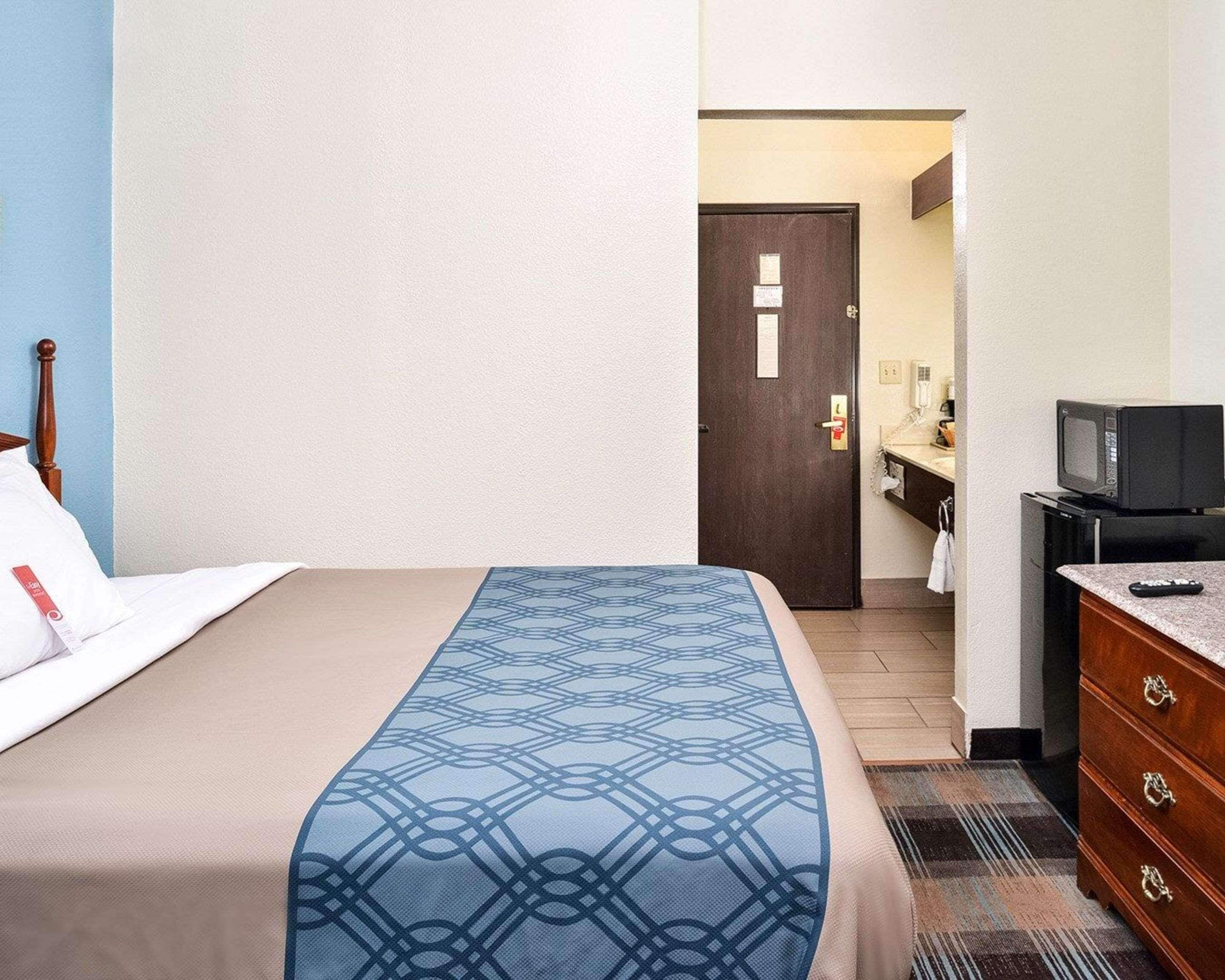 Habitación de hotel con cama, tocador, televisor y baño visible a través de una puerta abierta.