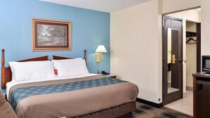 Quarto de hotel com cama, poltrona, abajur, quadro na parede e porta que dá para um corredor.
