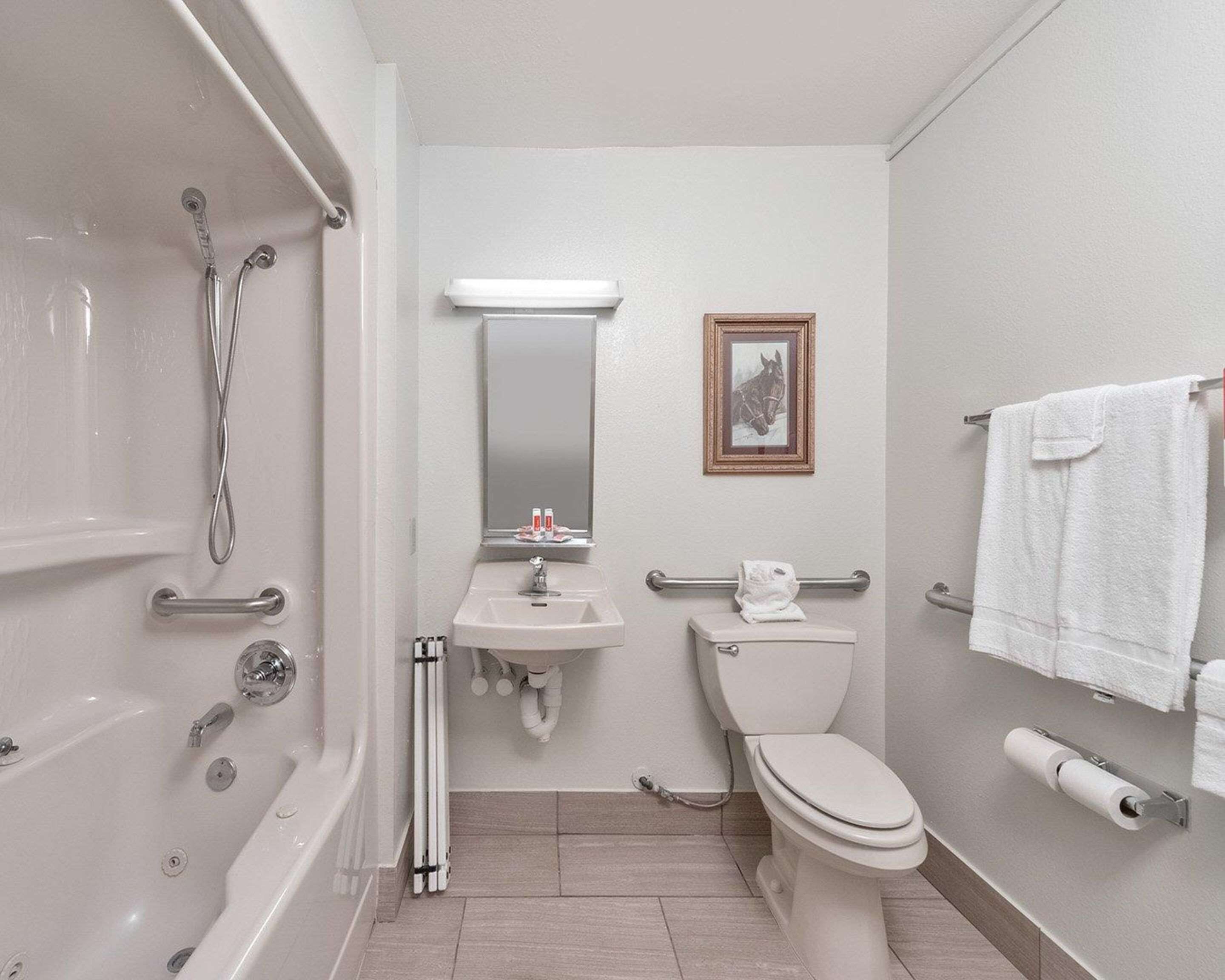 A modern bathroom with a bathtub, sink, toilet, and handrails.