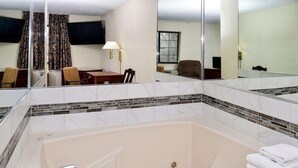 Um banheiro de hotel com uma banheira grande, um espelho e um espaço de estar com mesa e cadeiras.