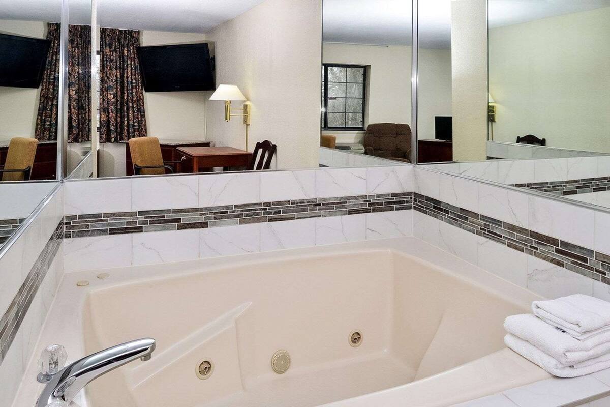 Une salle de bain d’hôtel avec une grande baignoire, un miroir et un coin salon comprenant une table et des chaises.