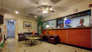 A lobby with a reception desk, seating area, ceiling fan, and a large plant. - Athens Hotel Suites (Houston)
