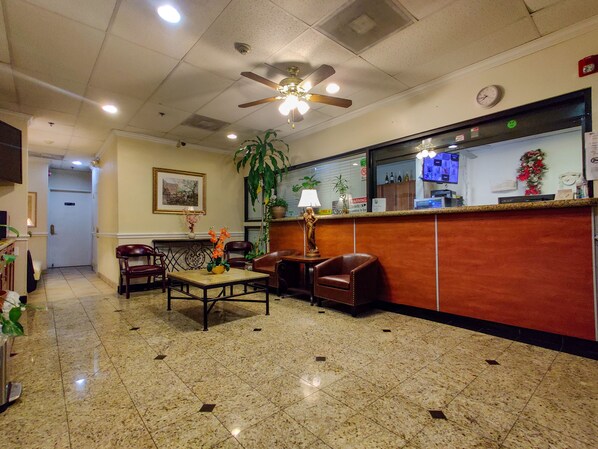 A lobby with a reception desk, seating area, ceiling fan, and a large plant. - Athens Hotel Suites (Houston)