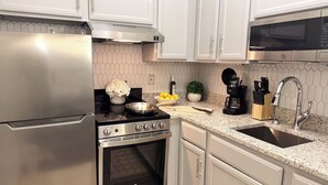 A modern kitchen with stainless steel appliances, white cabinetry, and a granite countertop. - Athens Hotel Suites (Houston)