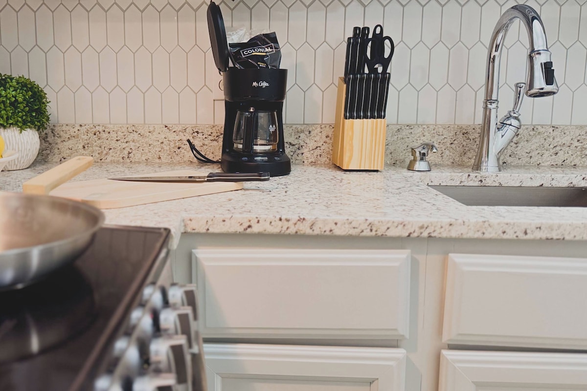 Una cocina con estufa, un bol de limones, cafetera y bloque de cuchillos.