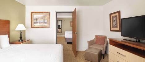 A hotel room with a bed, a TV, a desk, a chair, and a door leading to another room.