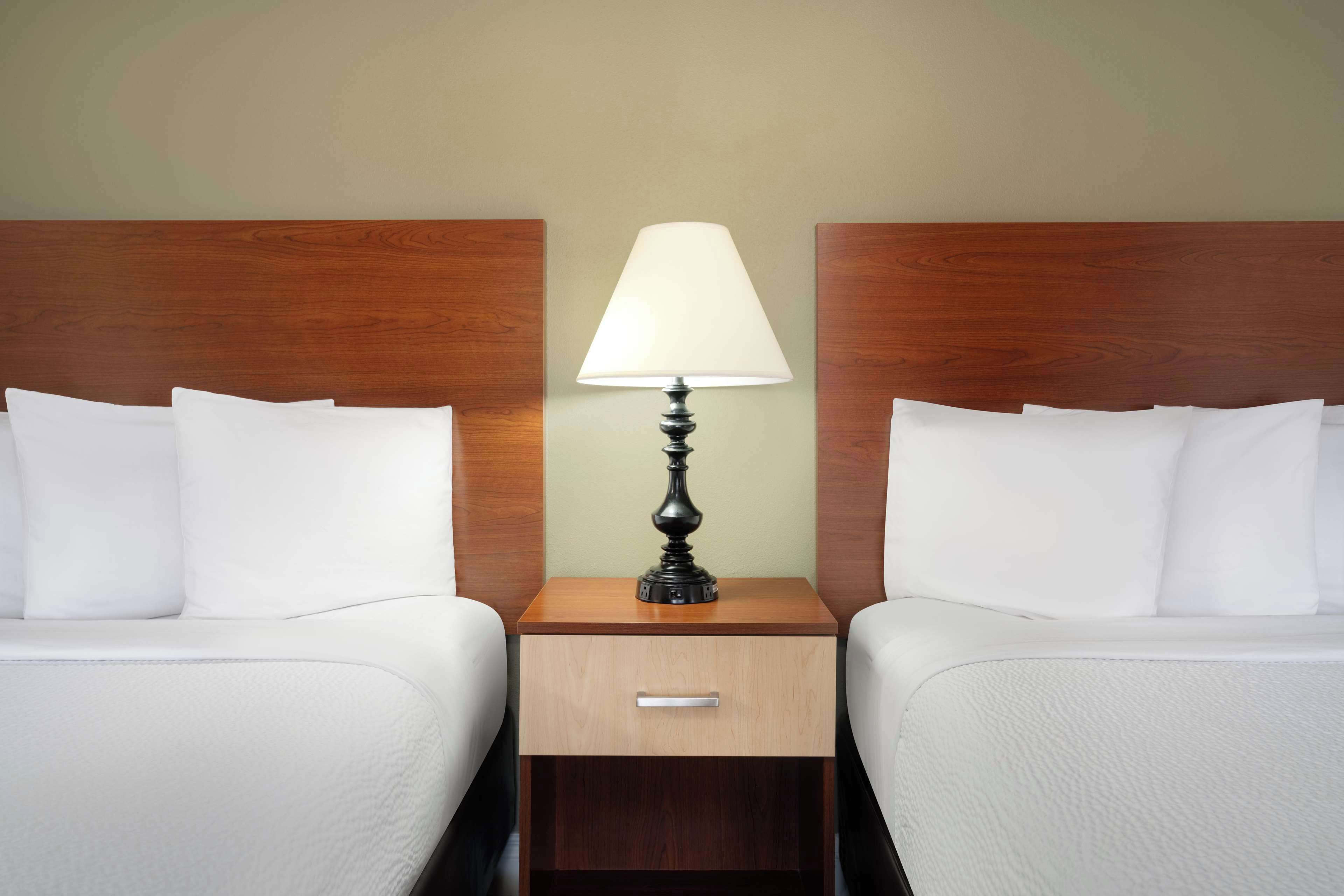 A hotel room with two single beds, a wooden nightstand with a lamp, and a small drawer.