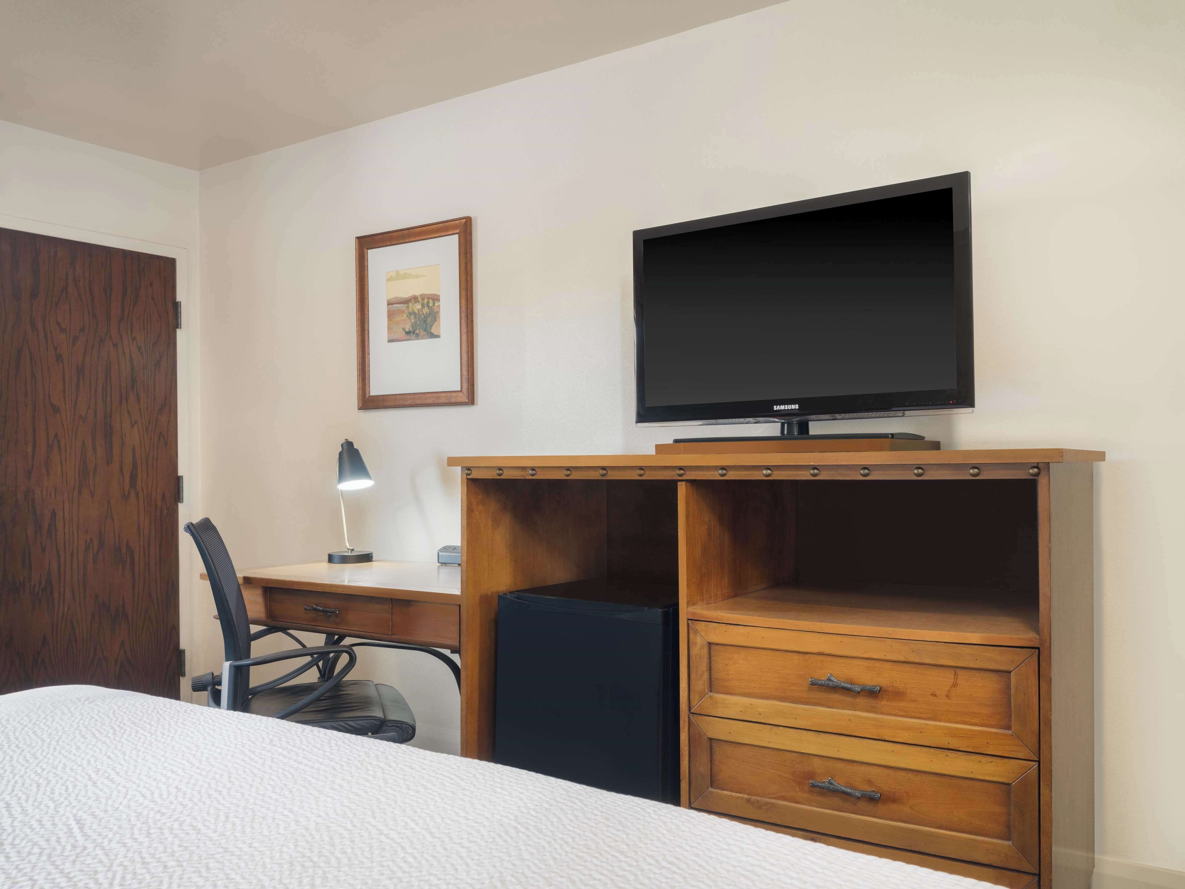 Une chambre d’hôtel comprenant un lit, un bureau avec une chaise, une télévision et une commode en bois.
