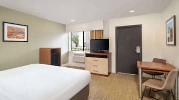 A hotel room with a bed, a desk with a chair, a television, and a wardrobe.