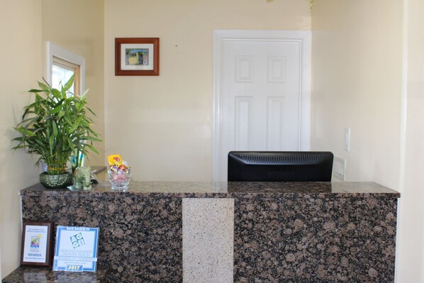 A reception desk with a framed membership sign, a potted plant, and a small vase with flowers.