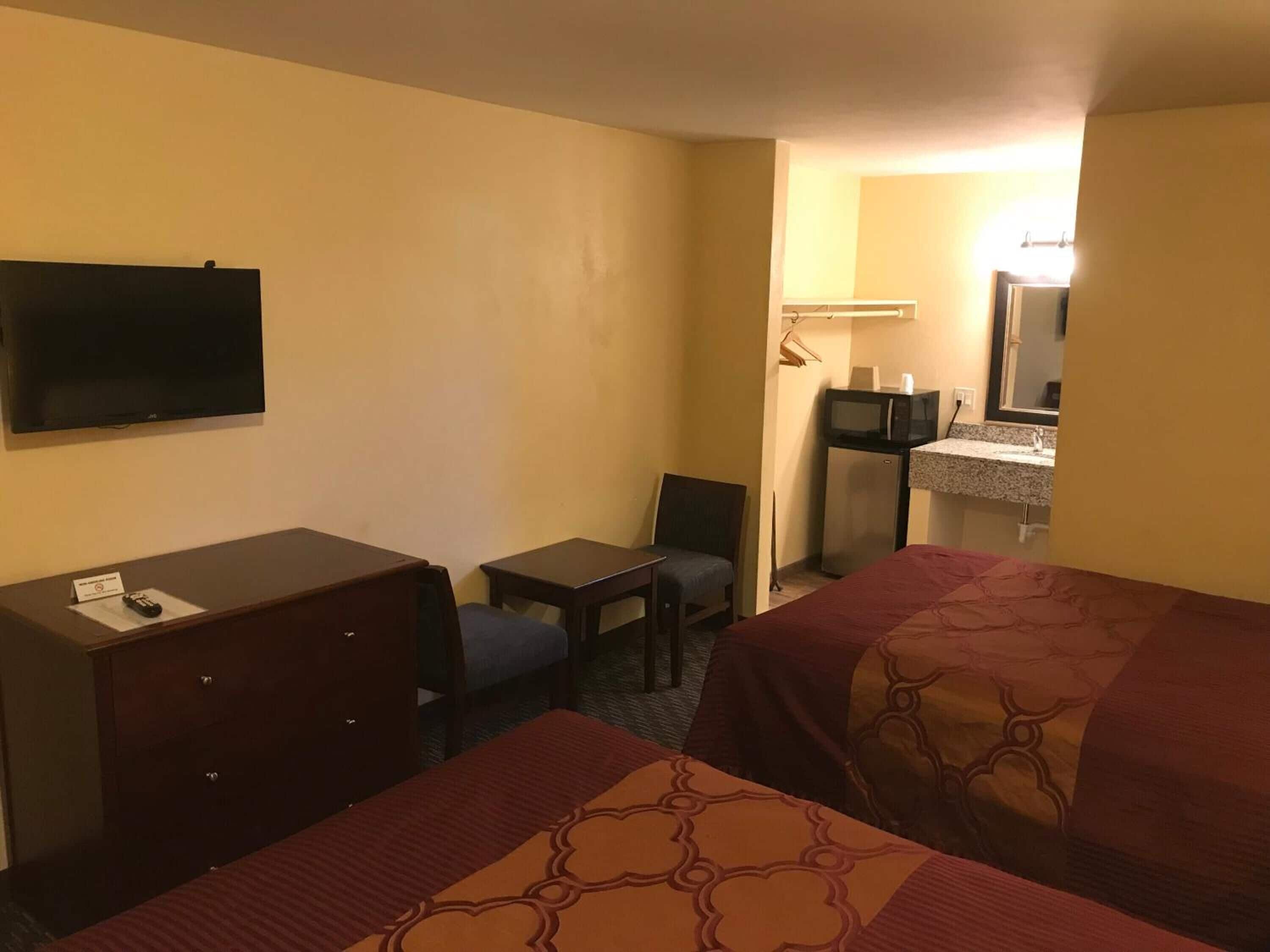 Habitación de hotel con dos camas, un escritorio, una silla, un televisor, un microondas y una mesita.