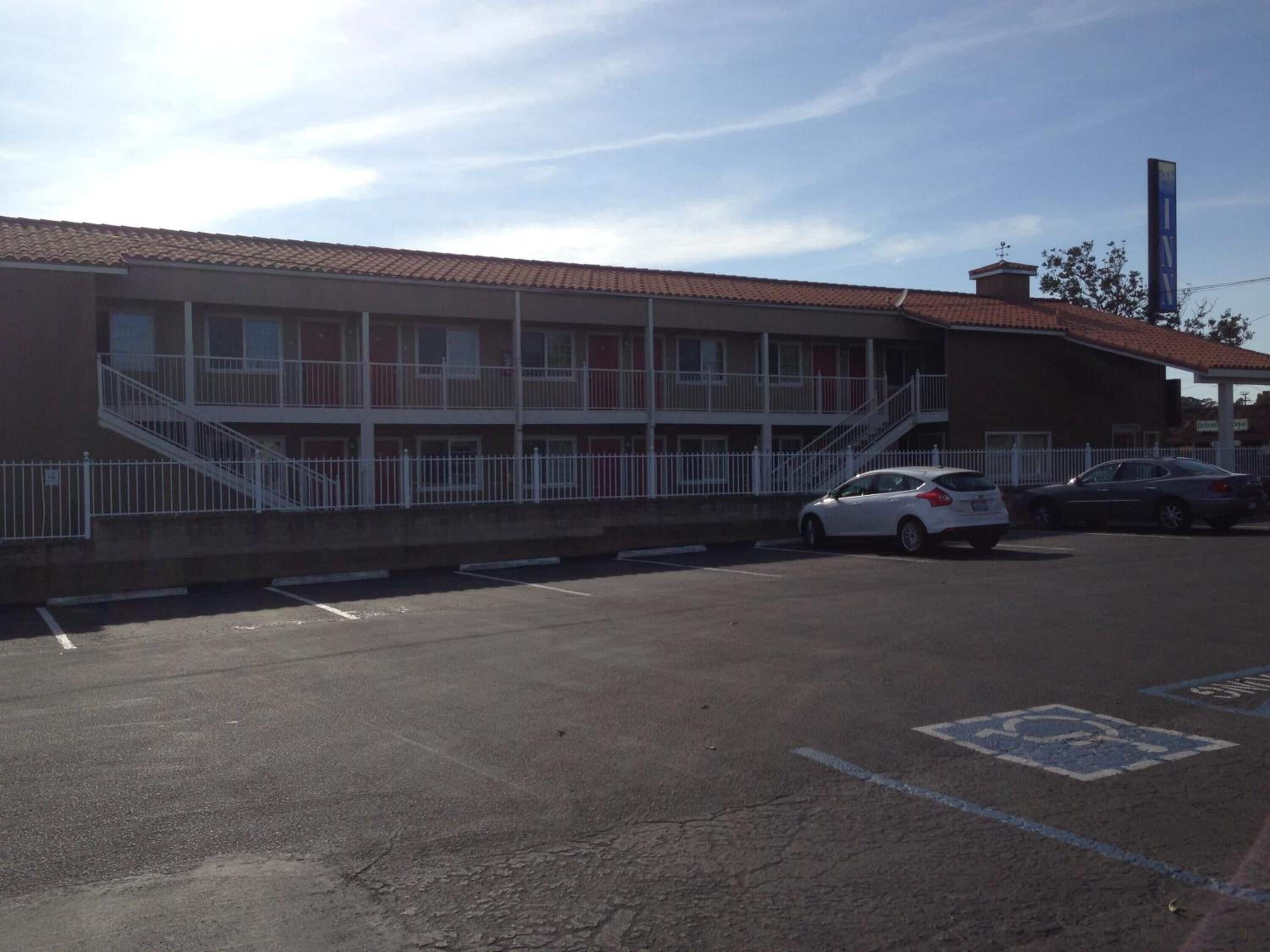 A building with a red-tiled roof, a white fence, and a parking lot with cars.
